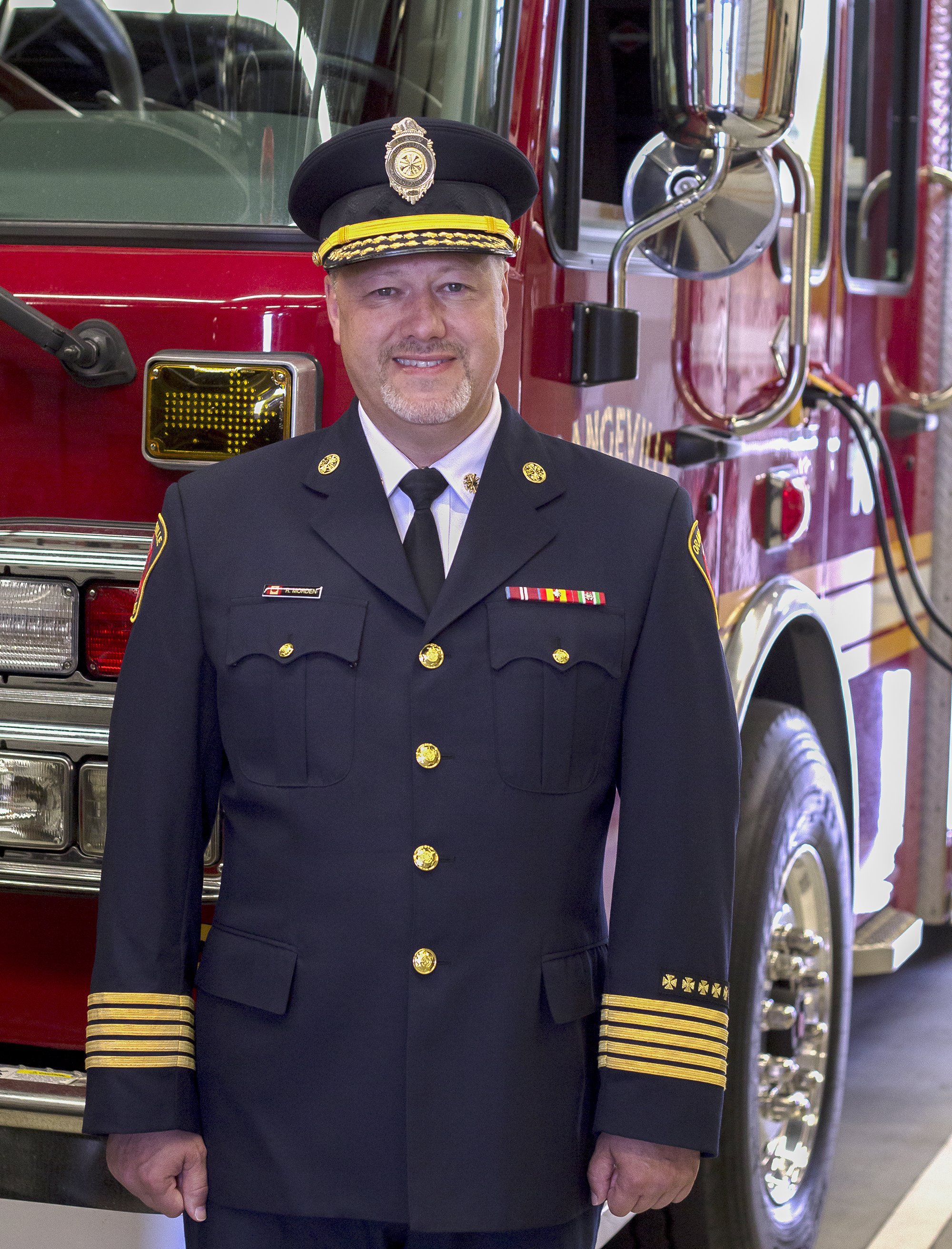 A photo of a fire chief standing in front of a fire truck.